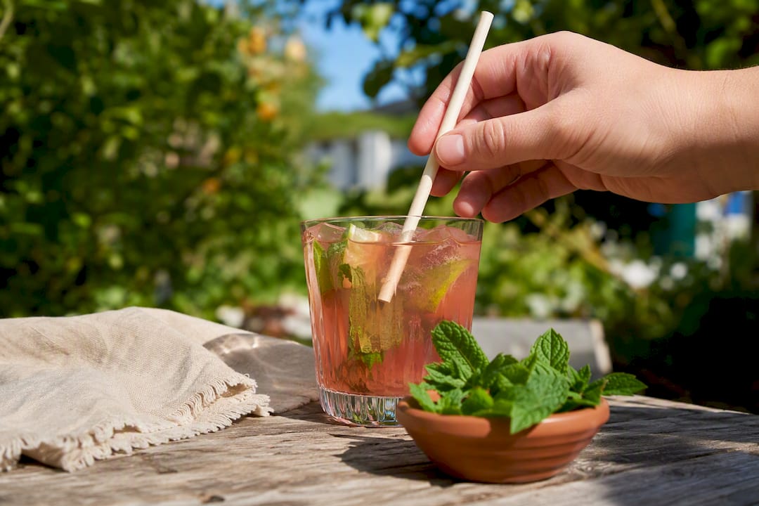 Hand die een composteerbaar rietje in een cocktailglas steekt